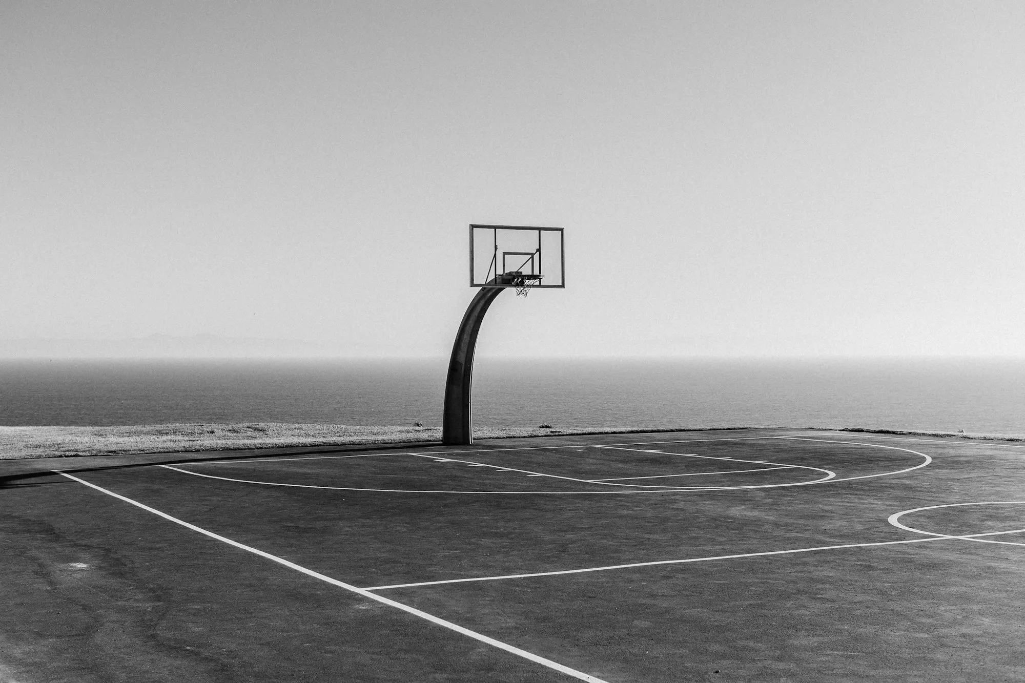 A lone basketball hoop on a court overlooking the water